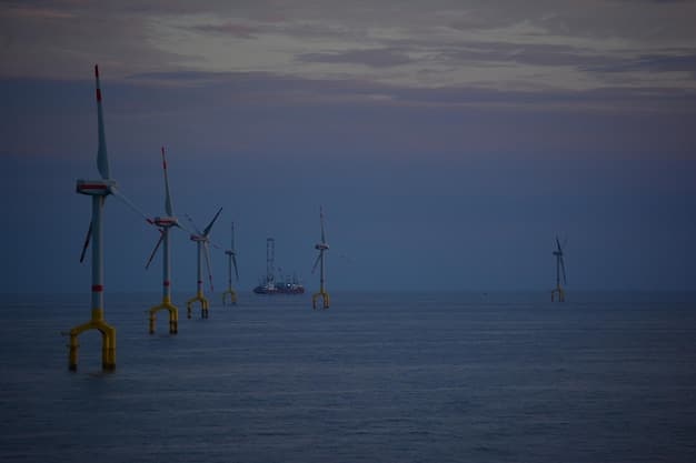 A fleet of advanced offshore wind turbines standing majestically in a twilight ocean, with a research vessel nearby, illustrating the scale and technological sophistication of modern wind power.