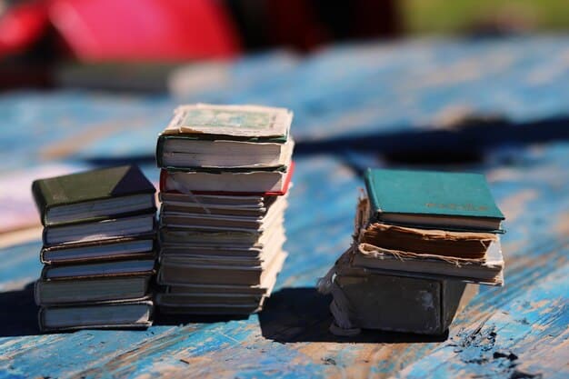A stack of neat, well-maintained used textbooks sits on a wooden table next to a laptop displaying a textbook buyback website. A 