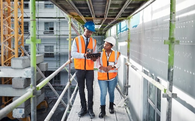 A team of engineers and construction workers in hard hats and safety vests reviewing blueprints at a busy construction site for a new bridge, with heavy machinery in the background.