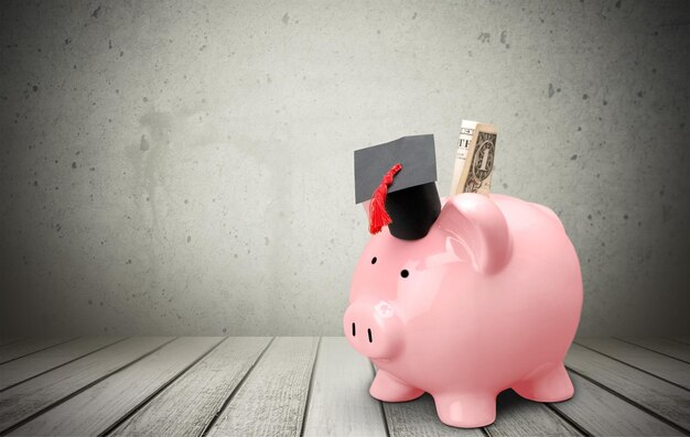 A piggy bank with a graduation cap on top, next to a small stack of money and a calculator, symbolizing future education savings.